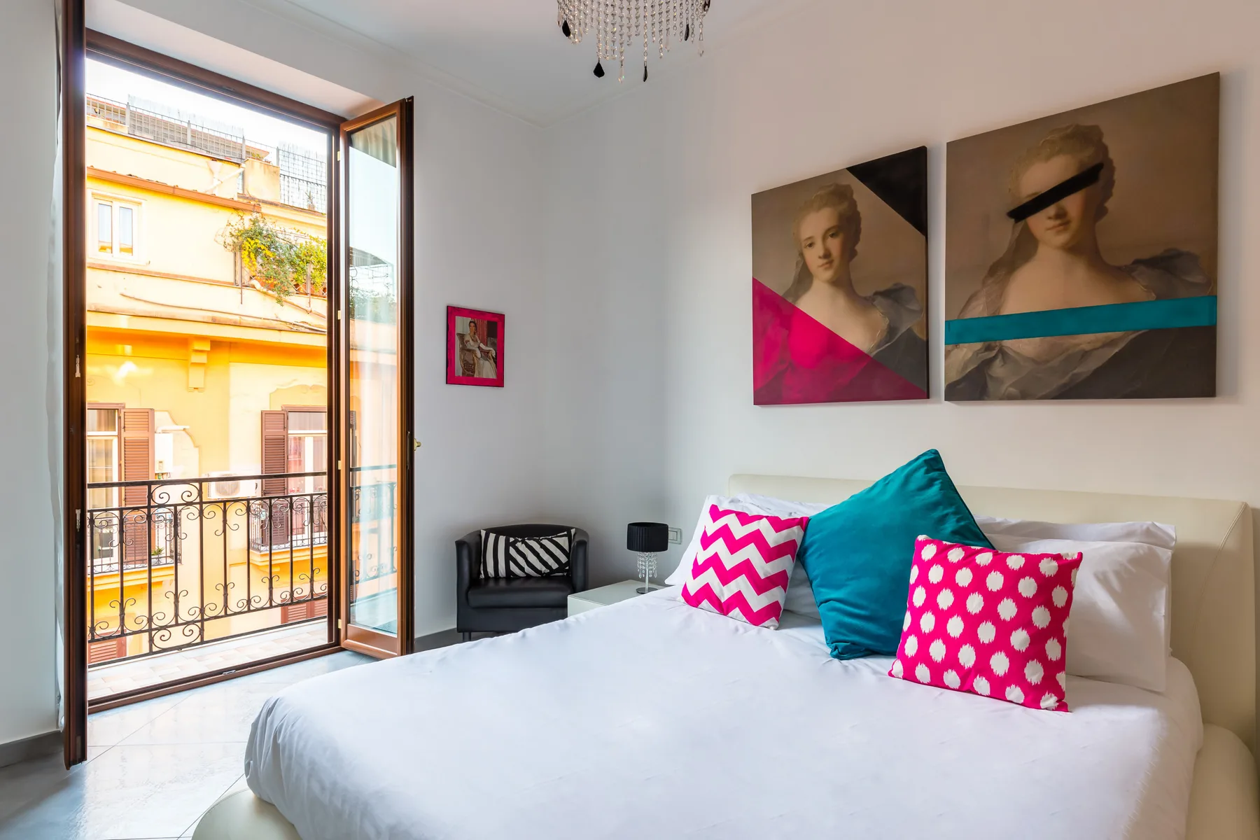 A bright bedroom with a white bed and colorful accent pillows beside an open balcony door.