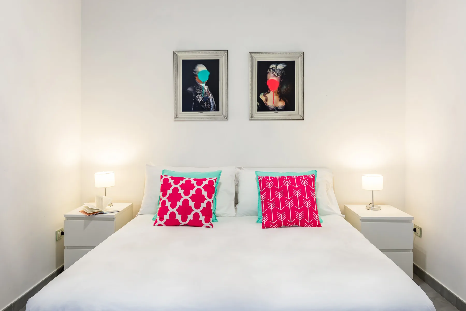 A bedroom with a neatly made bed and two bright pink accent pillows.