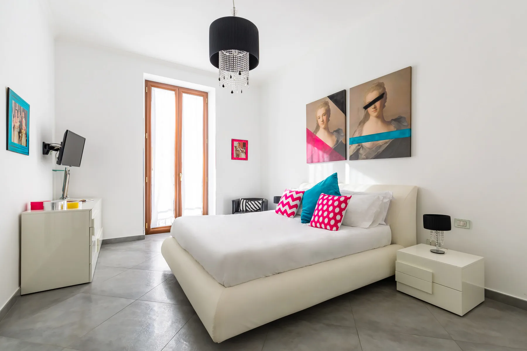 A bright bedroom features a large bed with colorful accent pillows and artwork above it.