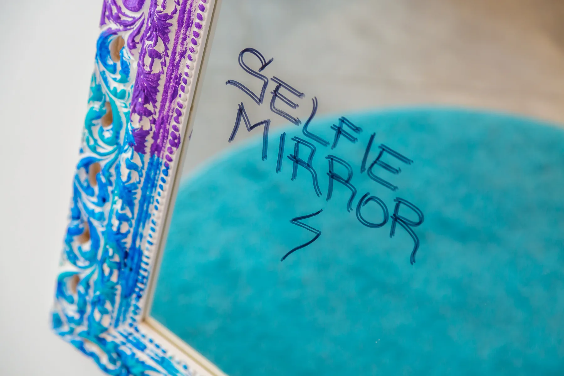 A decorative mirror with colorful ornate edging and handwritten lettering on its glass.