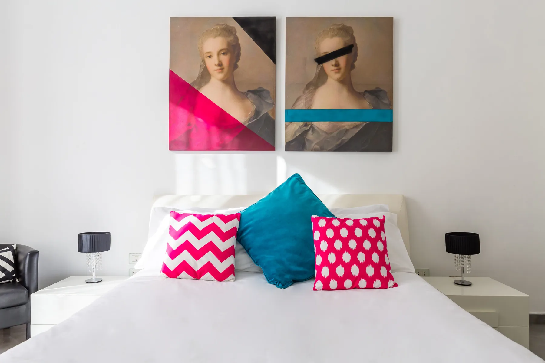 A bedroom with a white bed and bright patterned pillows beneath two portraits.