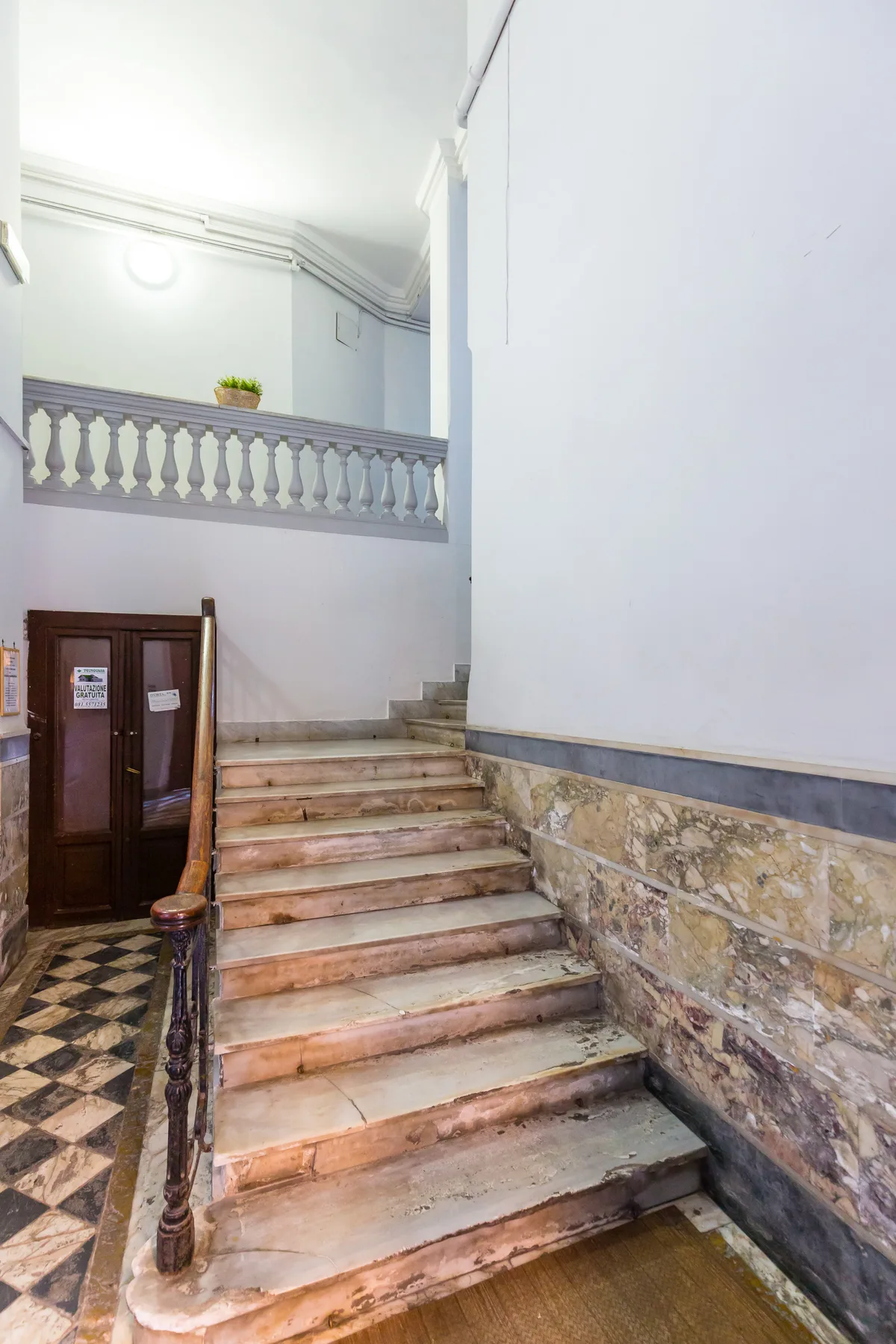 A stone staircase rises beside a dark wooden doorway in a pale interior.