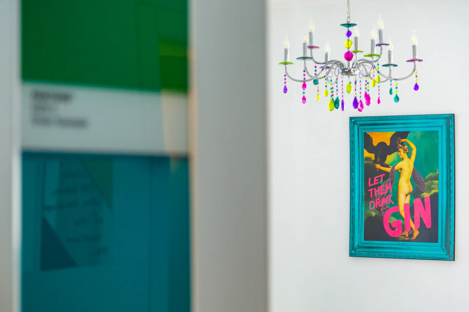 A colorful chandelier hangs above a framed poster on a white wall.