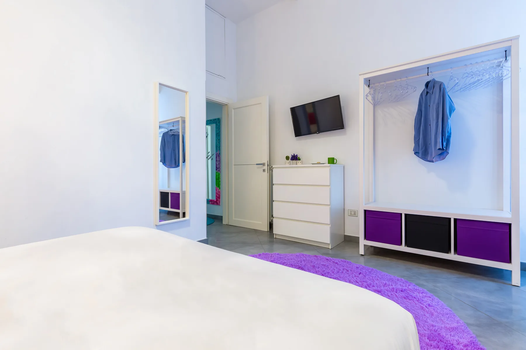 A bright bedroom with a bed, dresser, and open clothes rack.