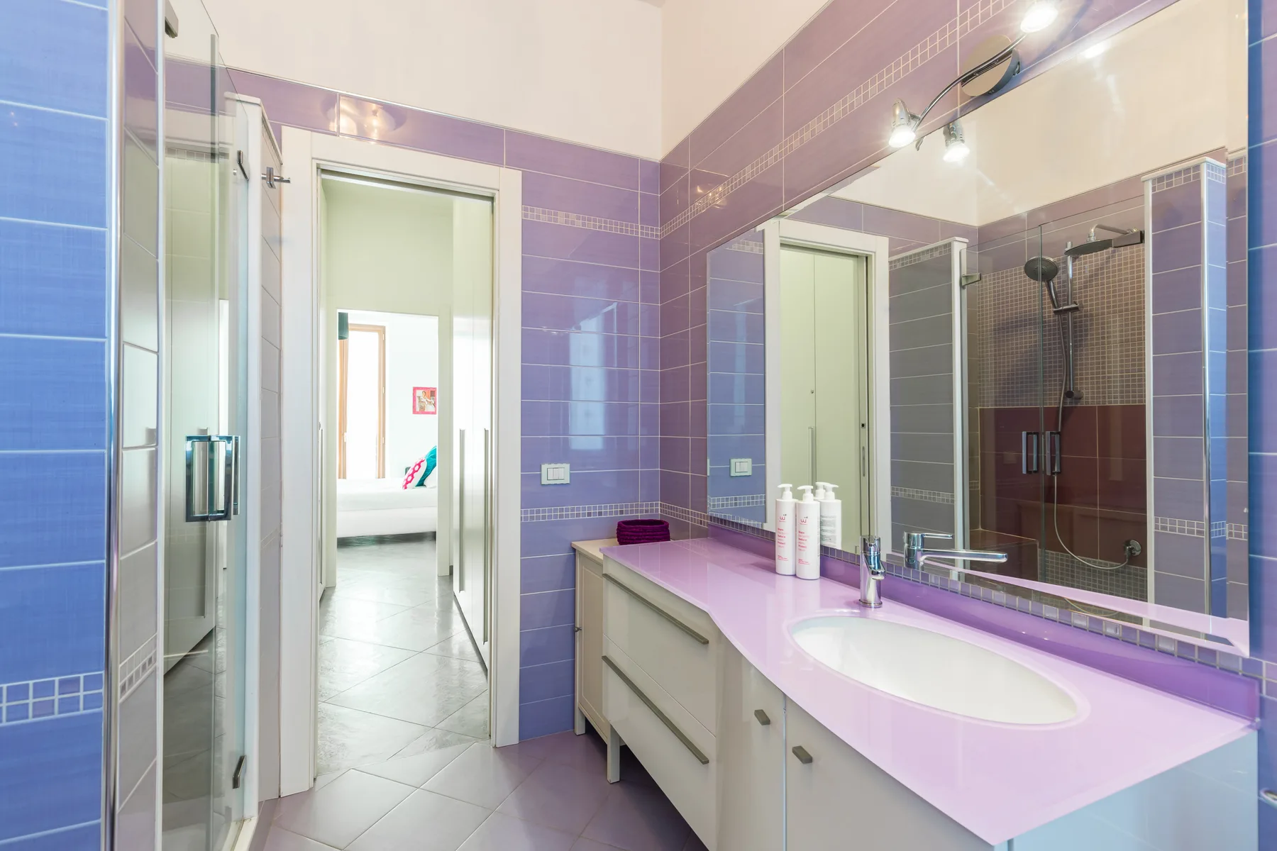 A tiled bathroom with a long vanity, sink, and large wall mirror.