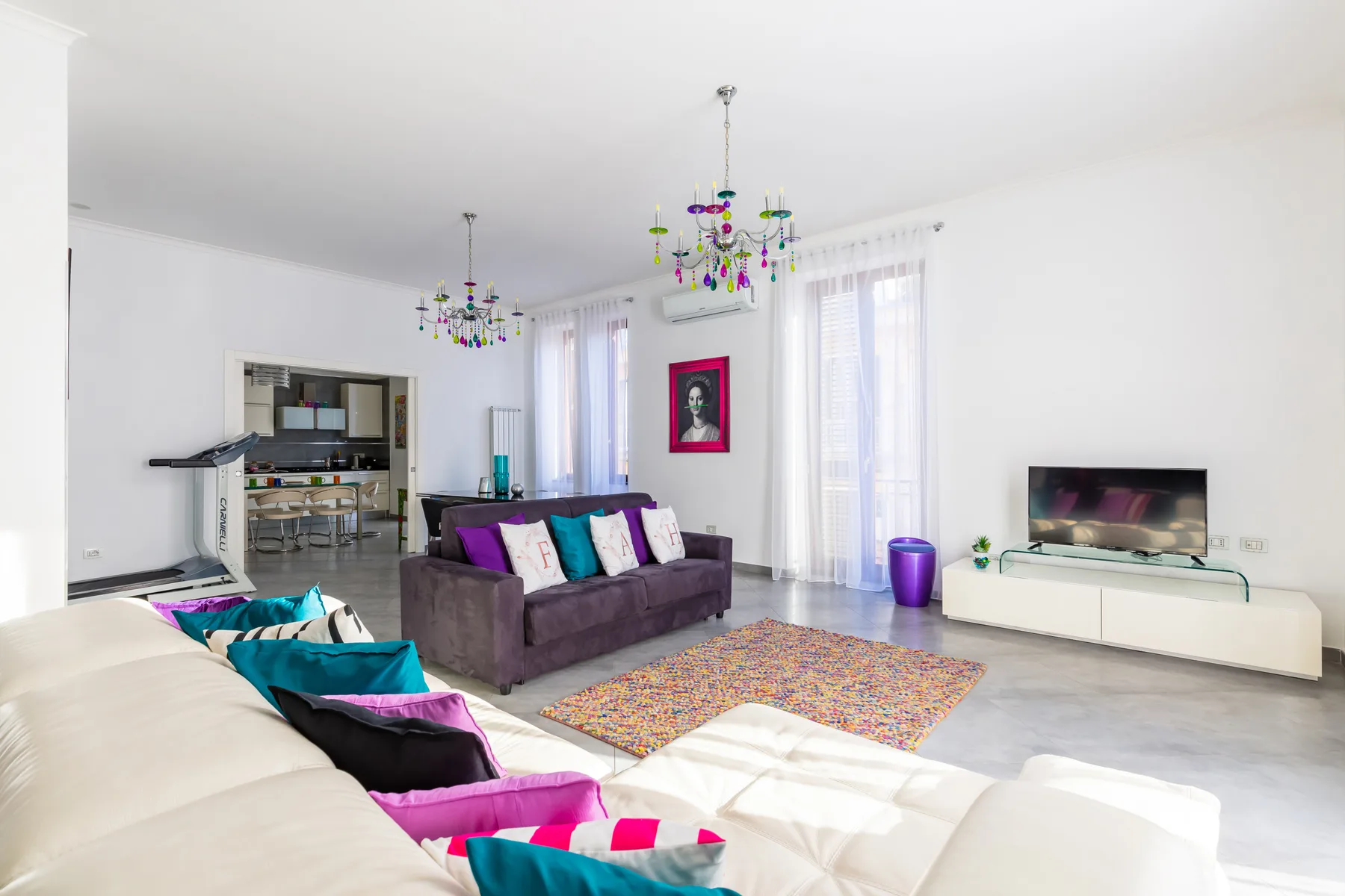 A bright living room with seating, colorful cushions, and a television.