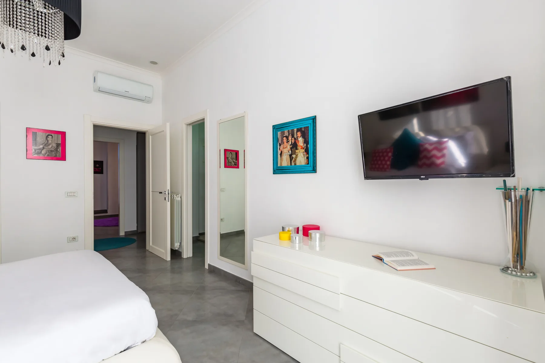 A bright bedroom with a bed, a wall-mounted television, and a white dresser.
