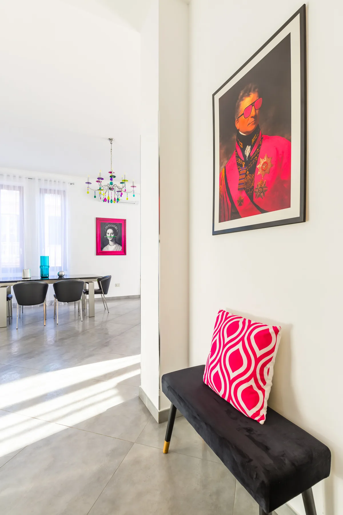 A bright dining area opens beside a narrow upholstered bench and colorful wall art.