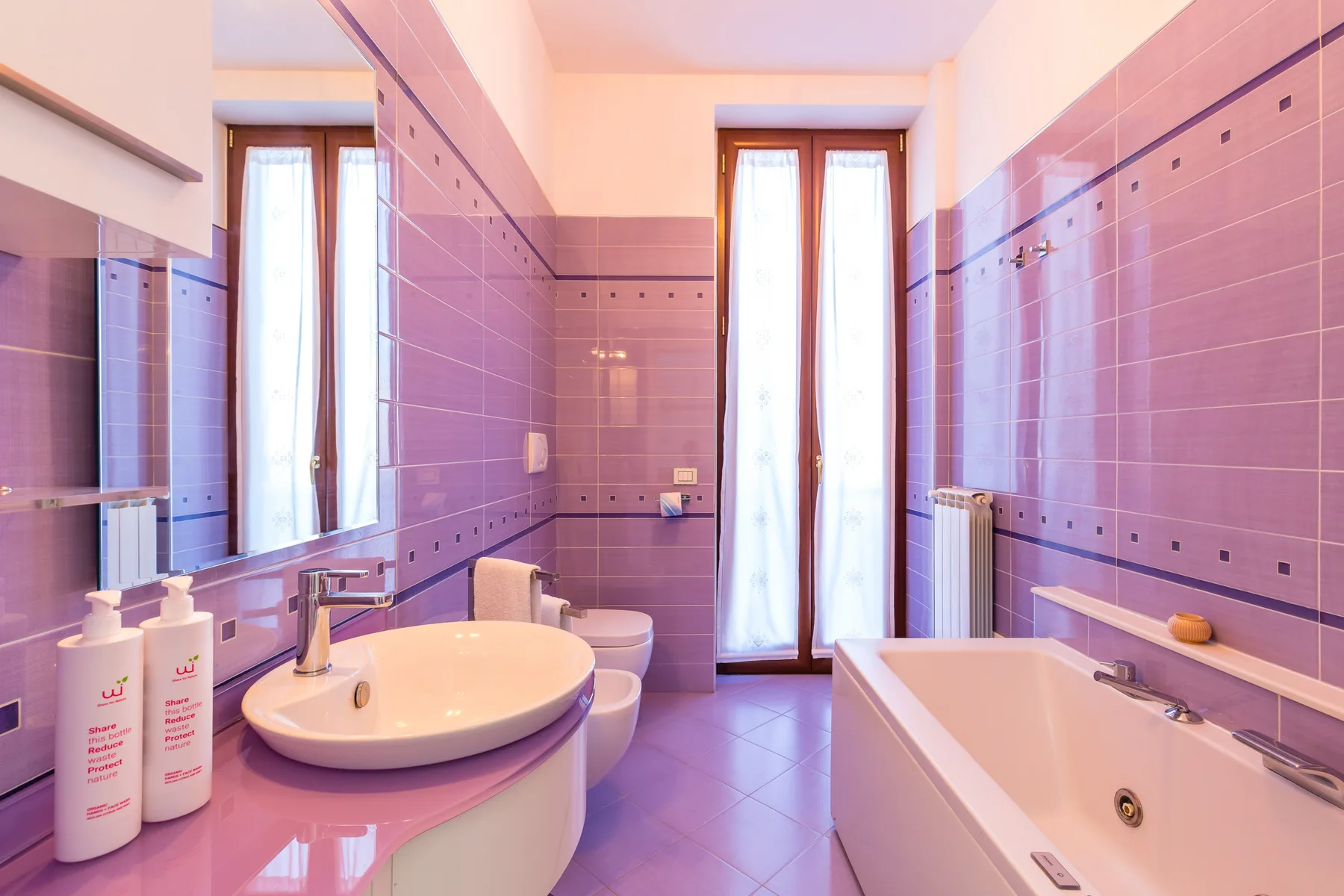 A bathroom with a sink and bathtub beside tall windows.