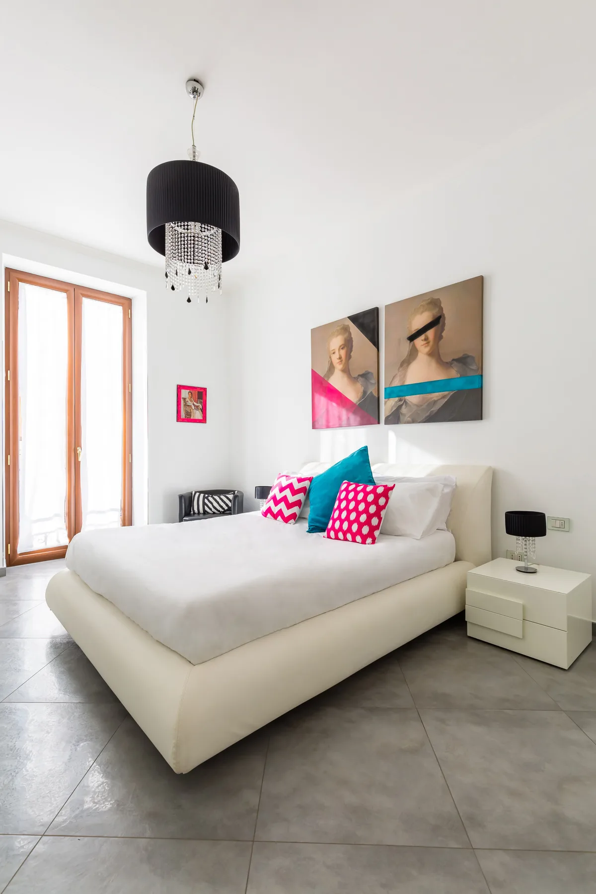 A bright bedroom with a large bed, colorful cushions, and wall art.