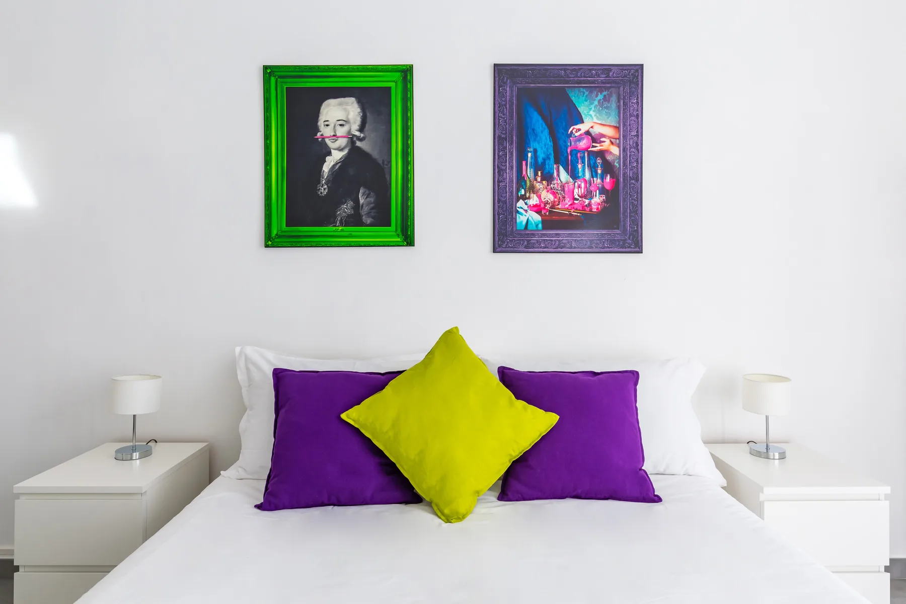 A bedroom with a bed, purple pillows, and colorful framed artwork.