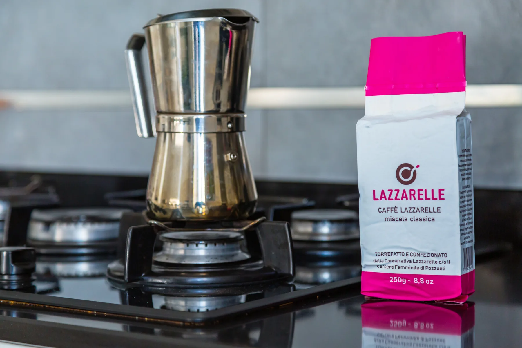 A moka pot and coffee package sit on a gas stovetop.