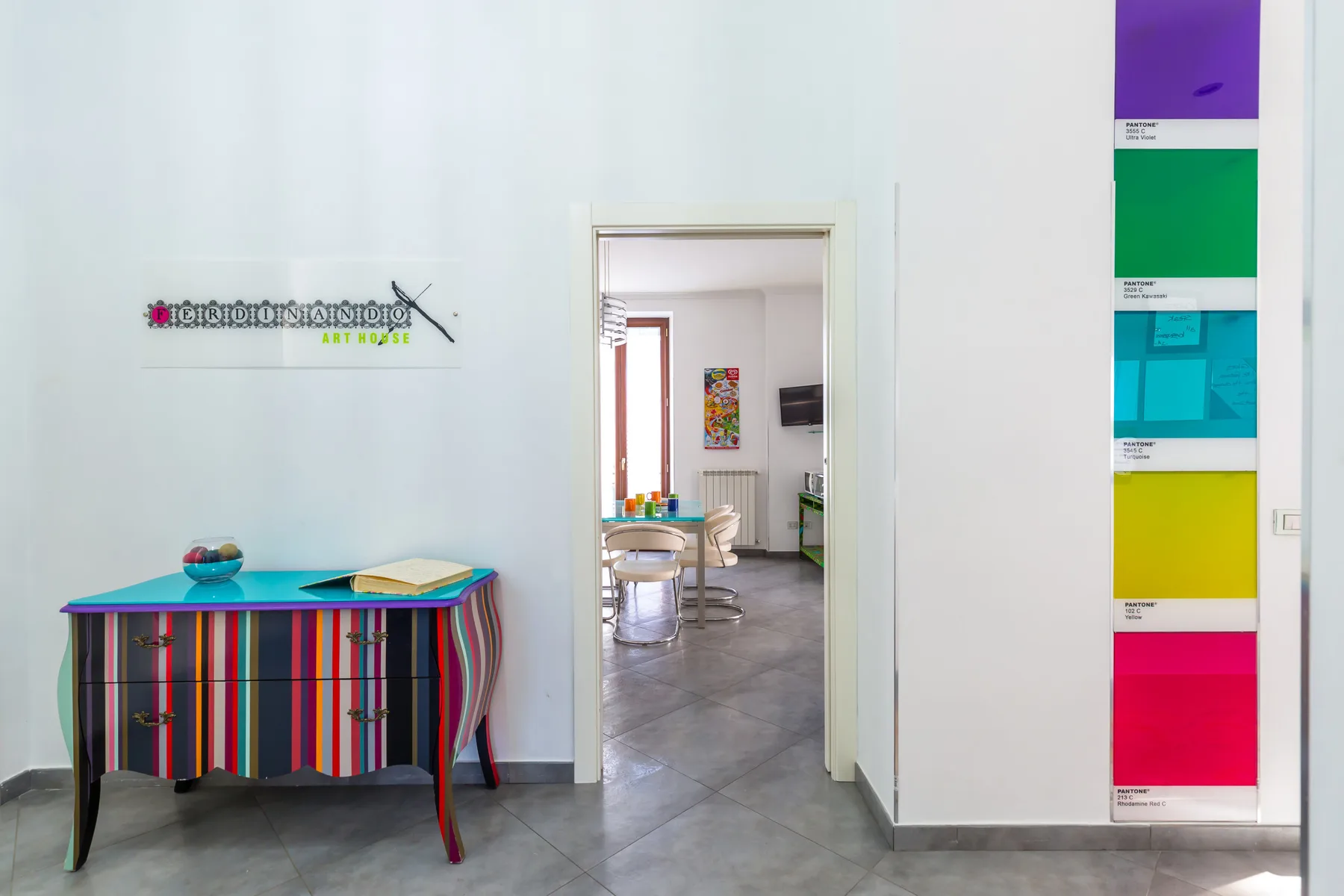 A colorful interior hallway opens into a bright room with a striped console table.