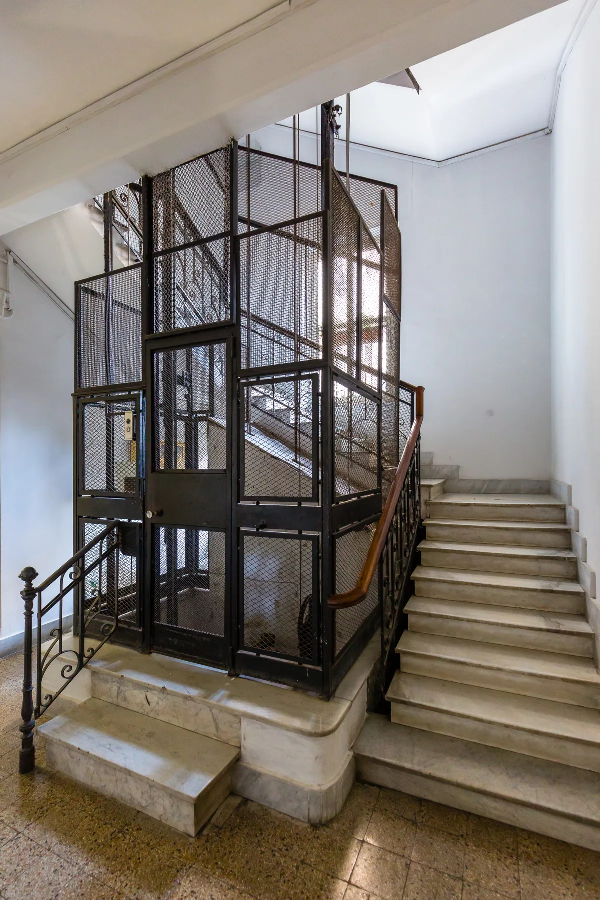 A staircase beside a tall metal lift enclosure with mesh panels.