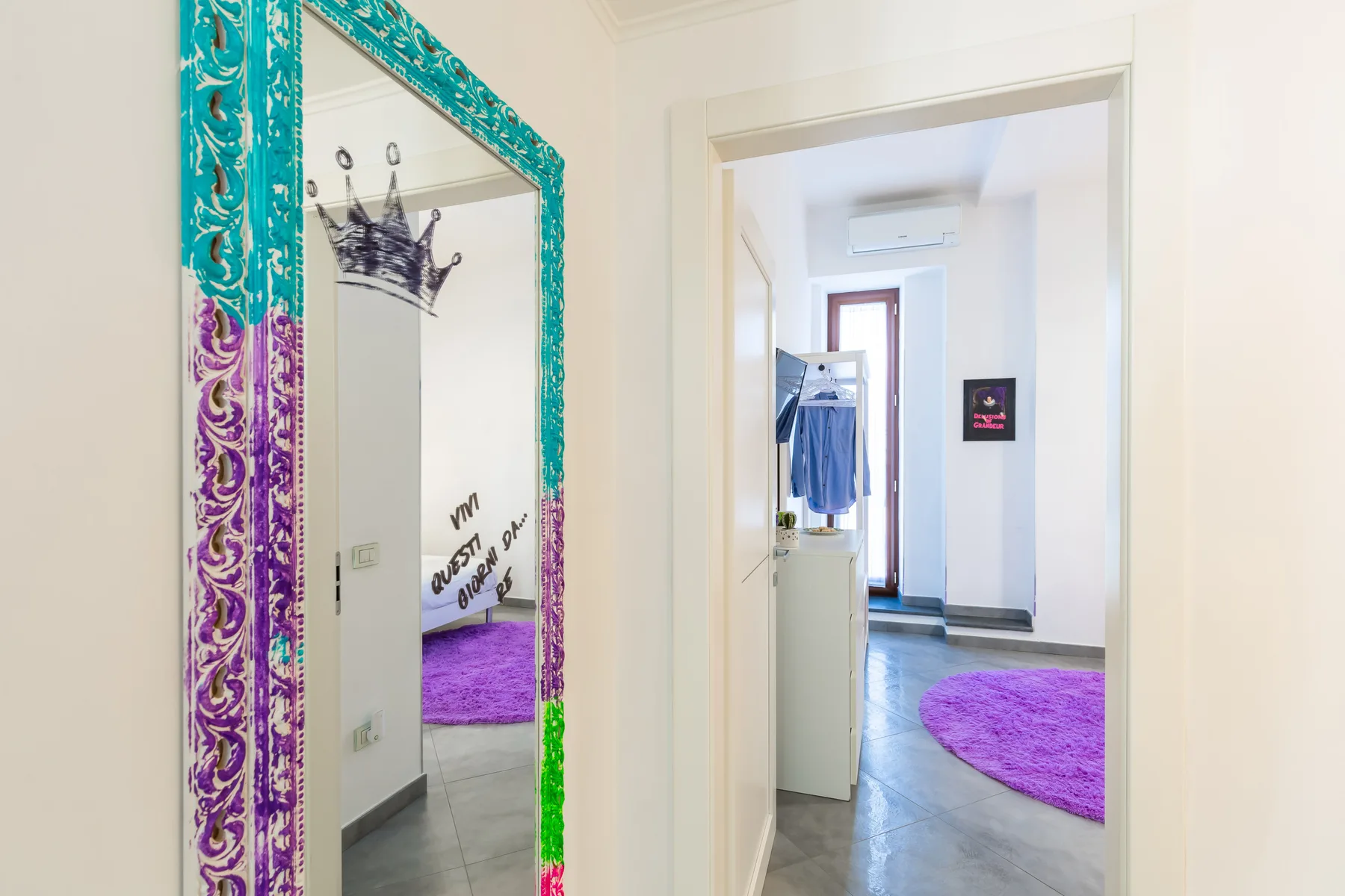 A bright hallway with a colorful framed mirror and a purple rug in the adjoining room.