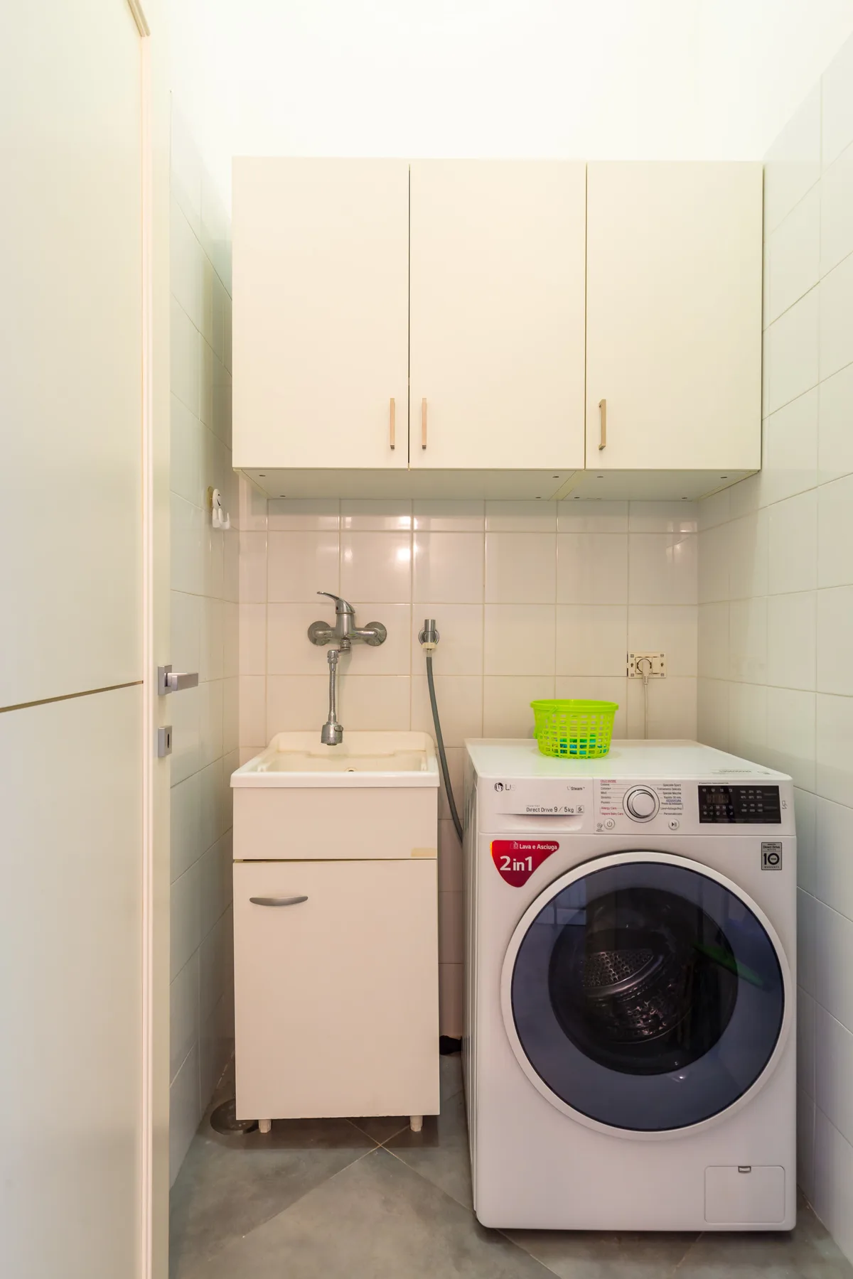 A compact laundry area with a washing machine, sink, and overhead cabinets.