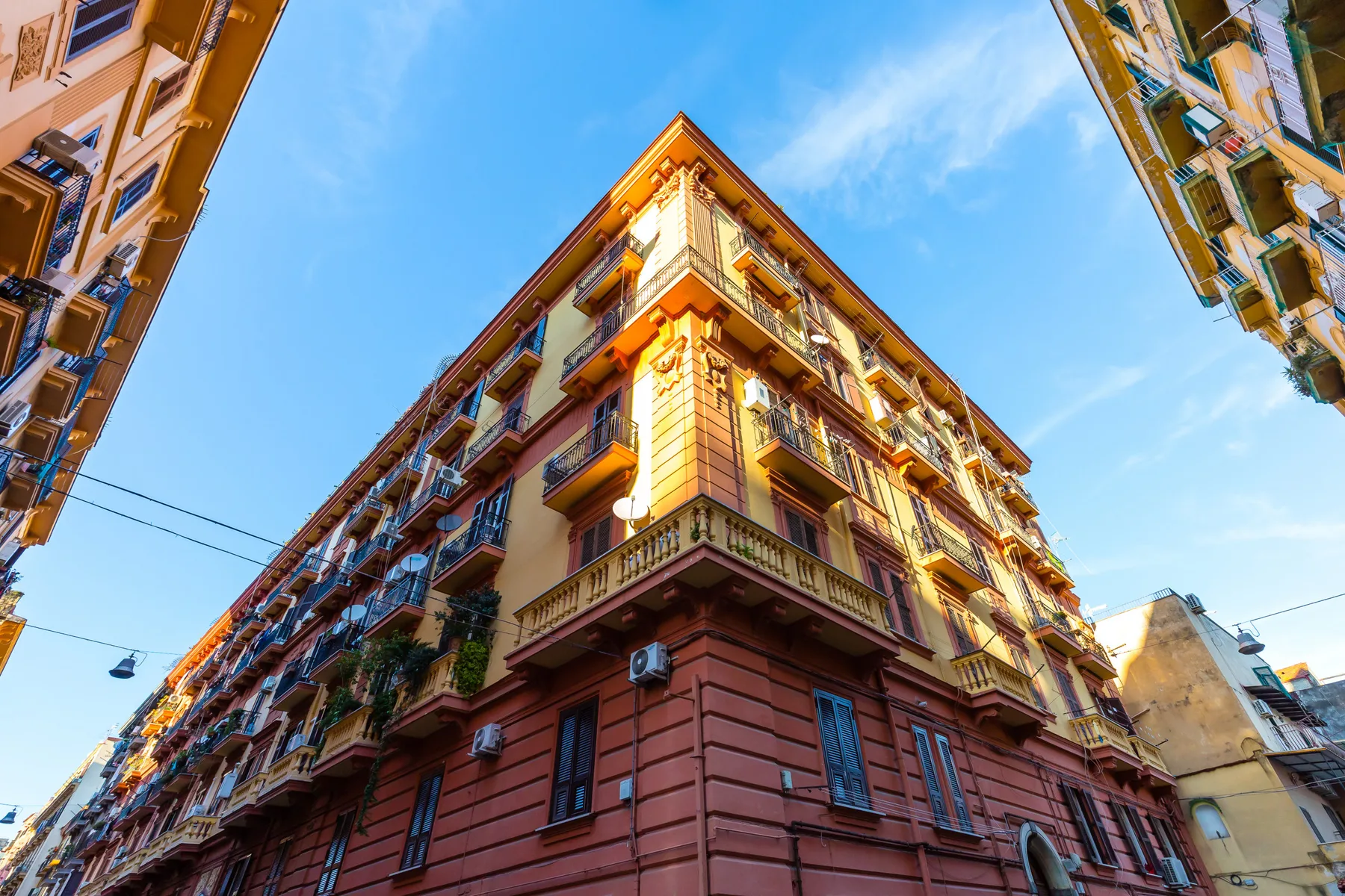 A sunlit multi-story apartment building rises above a narrow city street.