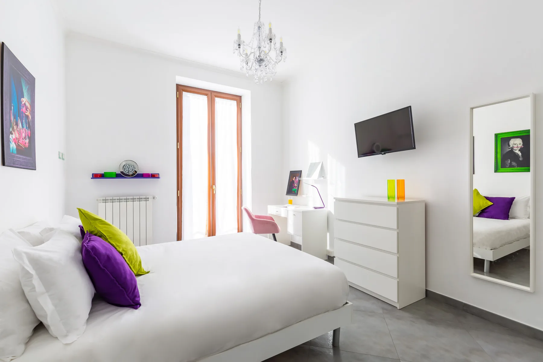 A bright bedroom with a bed, a dresser, and a wall-mounted television.