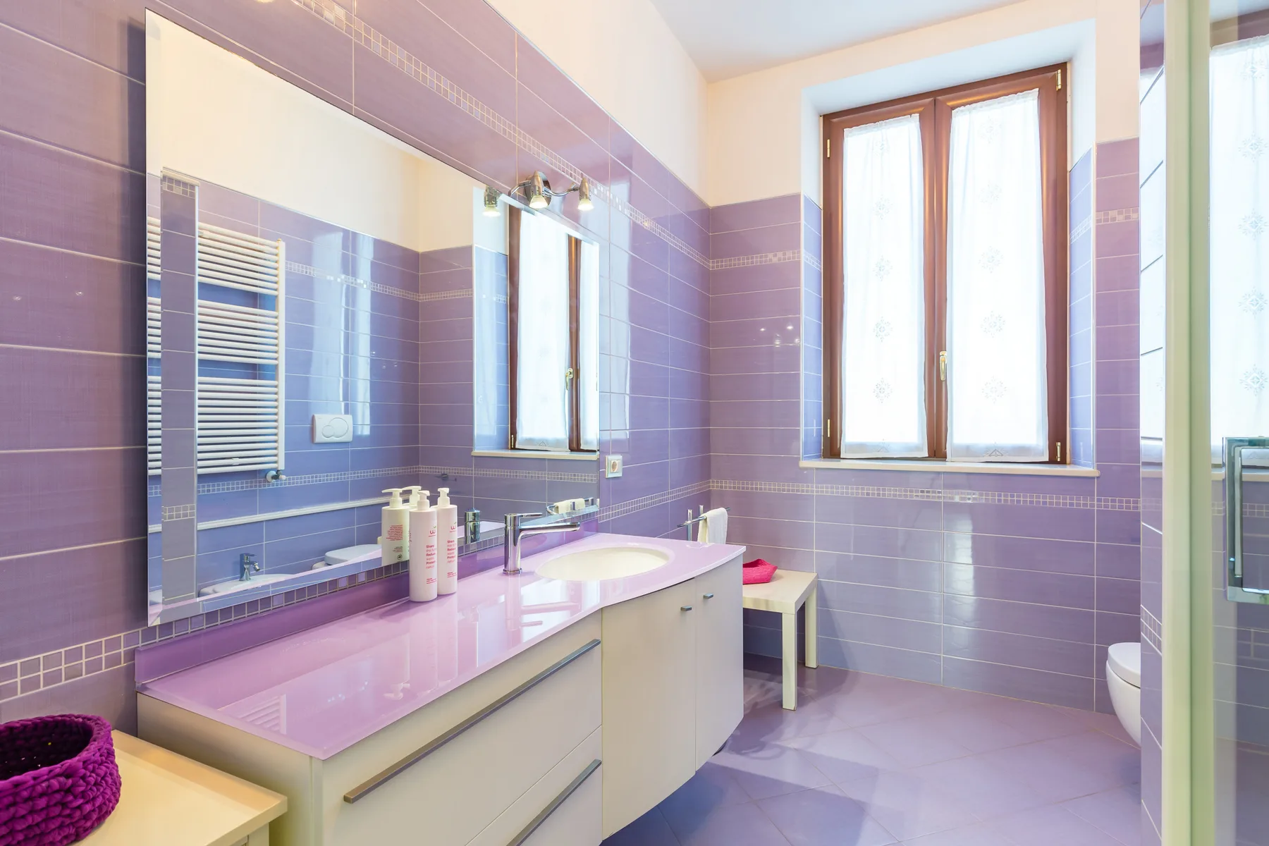 A tiled bathroom with a long vanity, mirror, and large window.