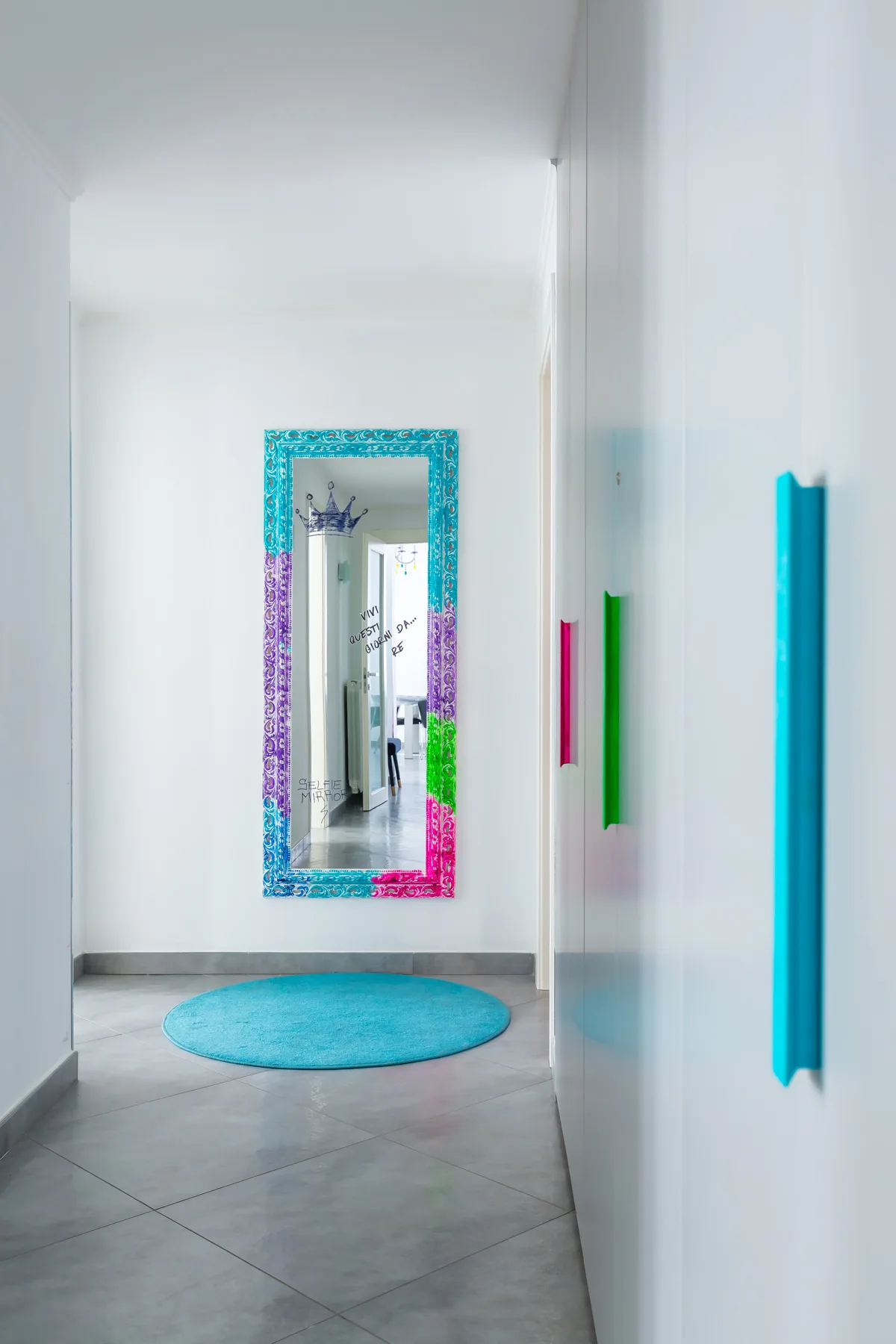 A bright hallway with a colorful framed mirror and a round blue rug.