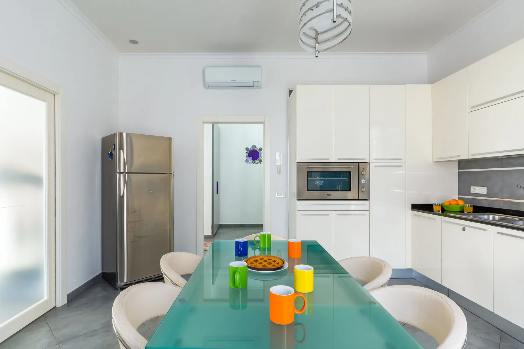 A bright kitchen and dining area with a glass table and white cabinetry.