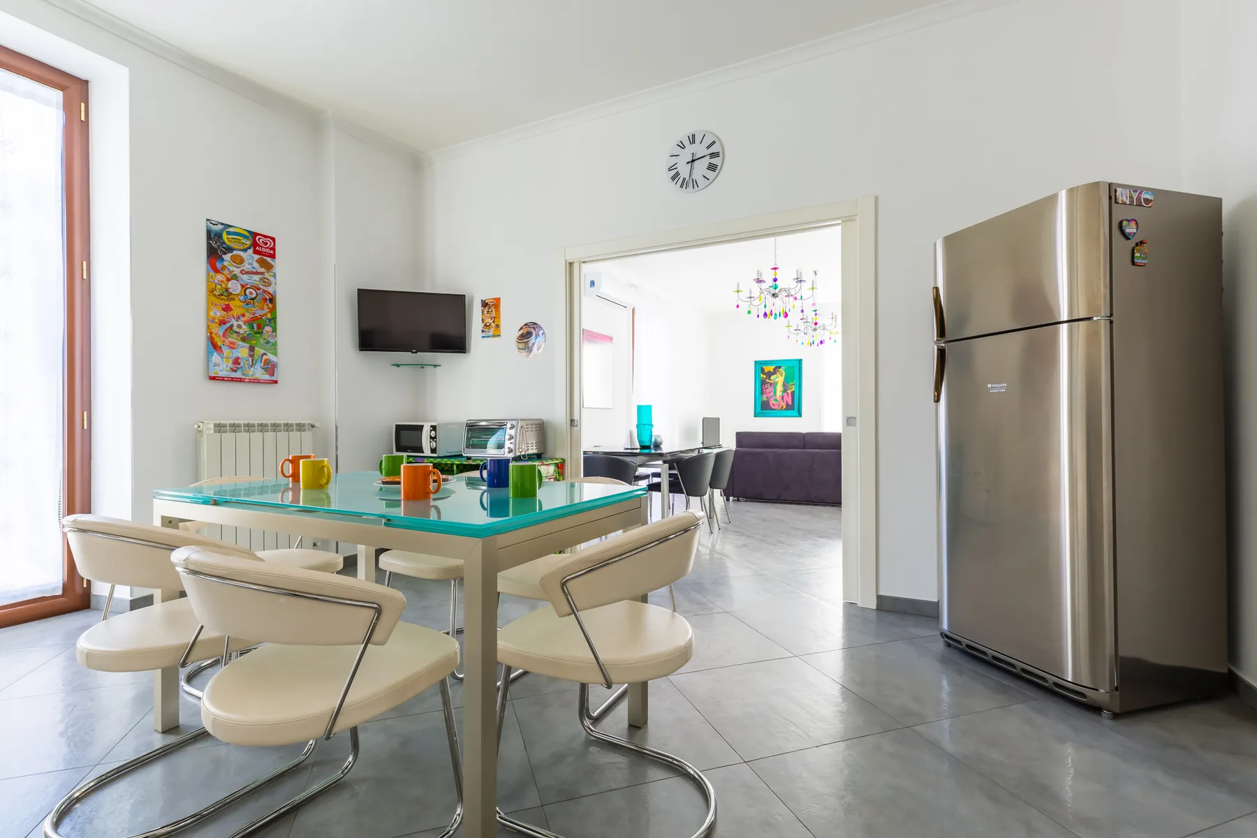 A bright dining area with a glass table and a kitchen refrigerator.