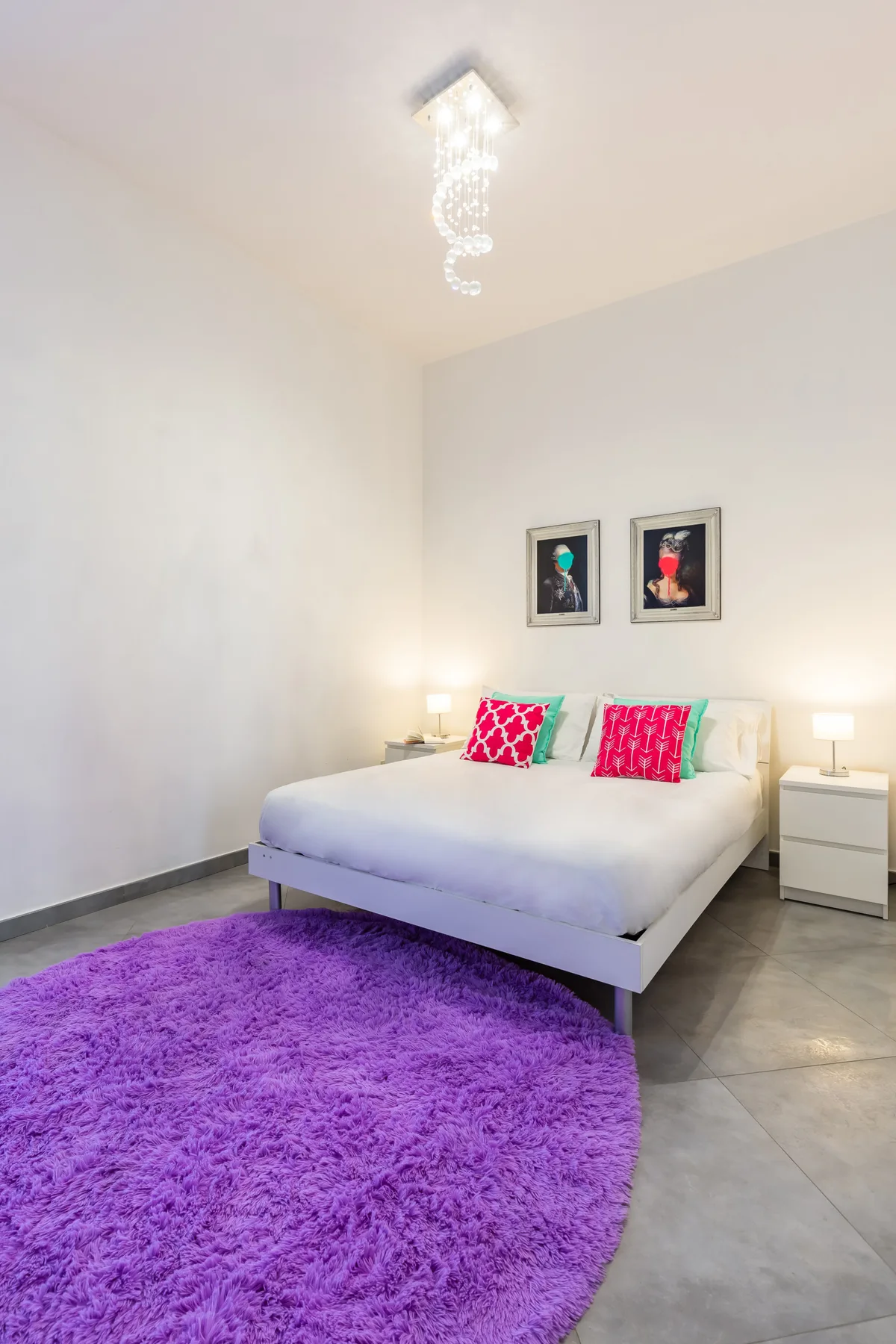 A bedroom with a white bed, colorful pillows, and a purple rug.