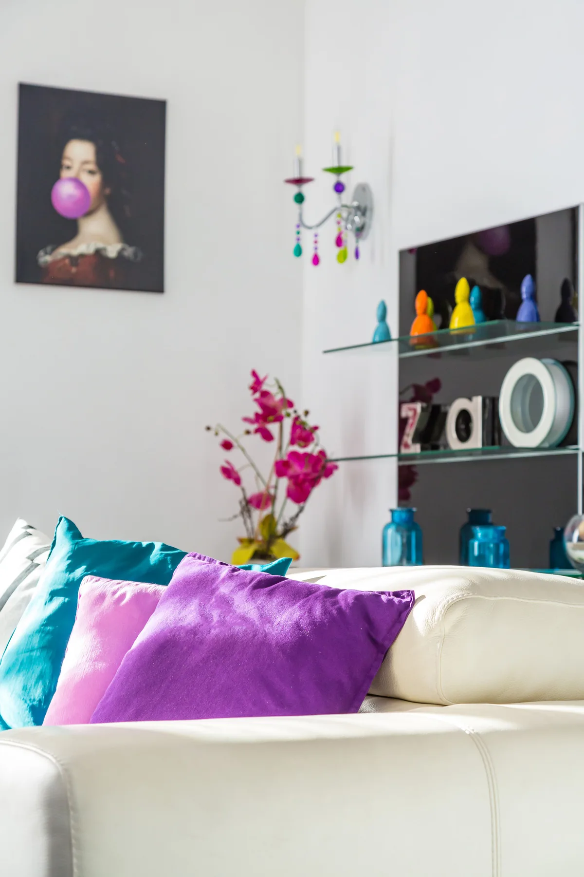 A bright living room with a cream sofa, colorful cushions, and wall shelving.