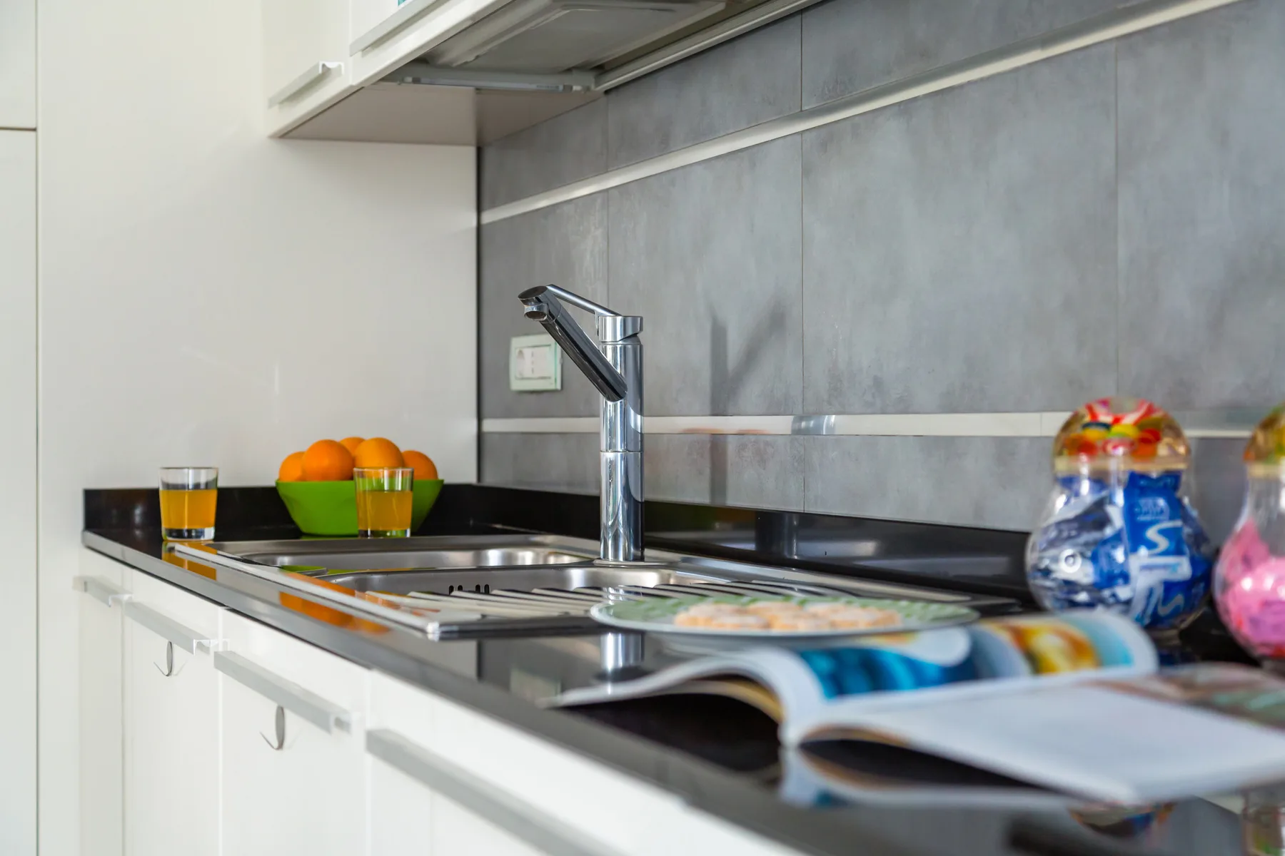 A kitchen counter with a sink, faucet, and bowl of oranges.