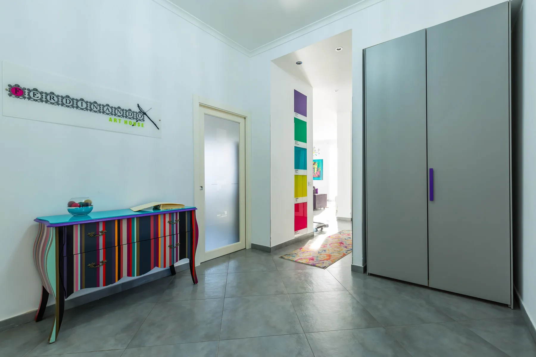 A bright hallway with a colorful striped console table and a large gray cabinet.