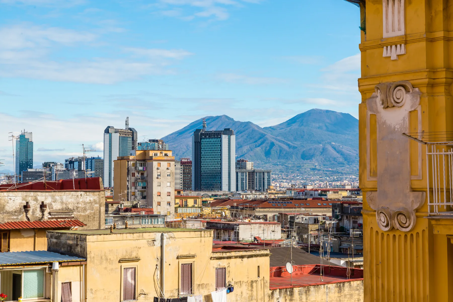 A city skyline with mountains in the distance, viewed beside an ornate yellow facade.