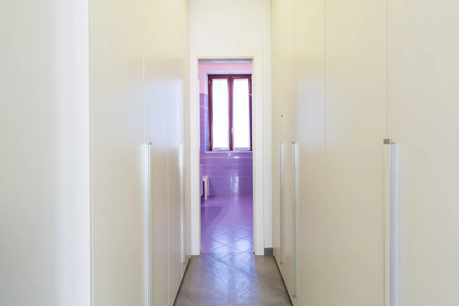 A narrow hallway leads to a room with a window at the far end.
