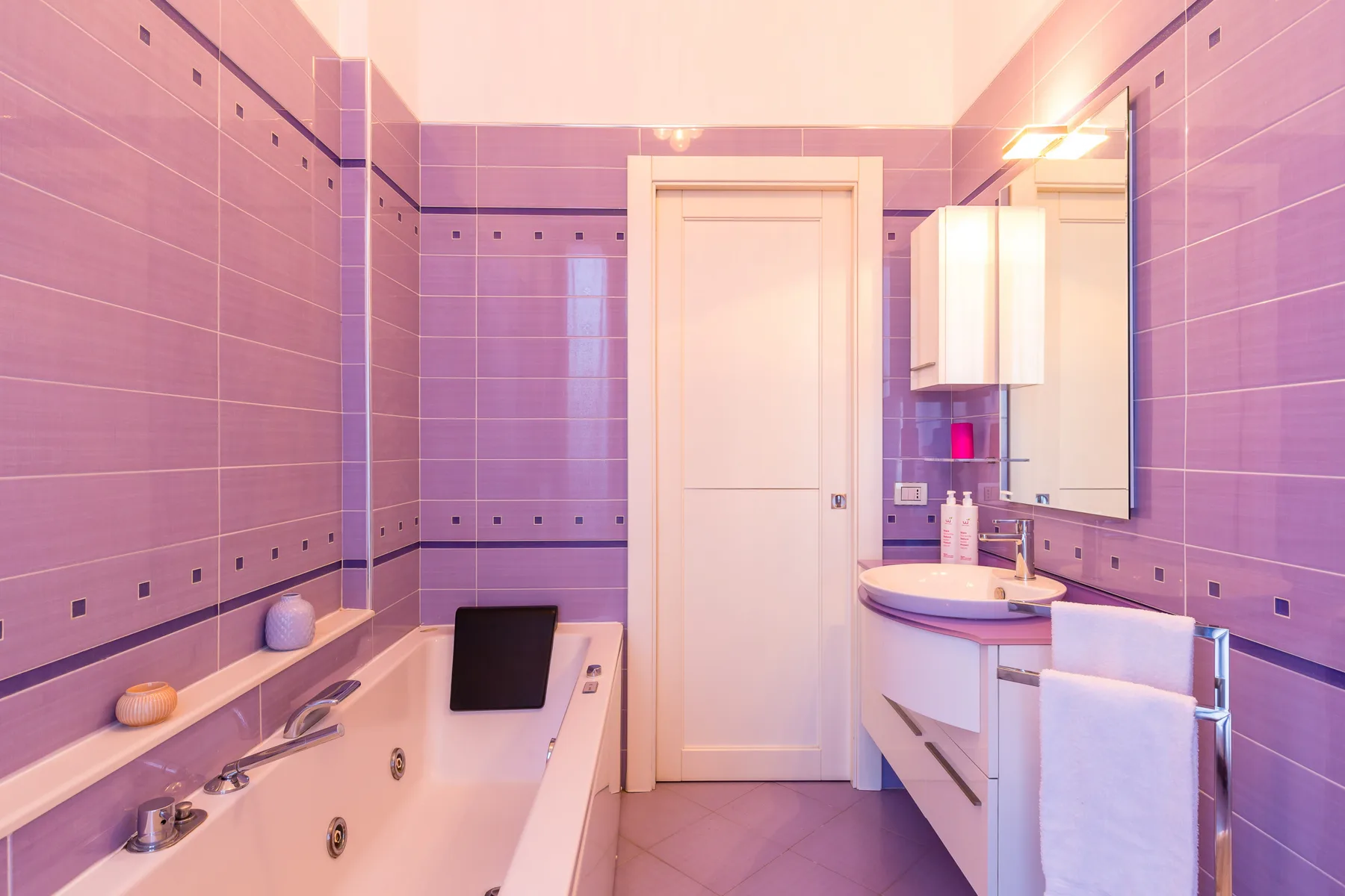 A tiled bathroom with a bathtub, sink, and wall mirror.
