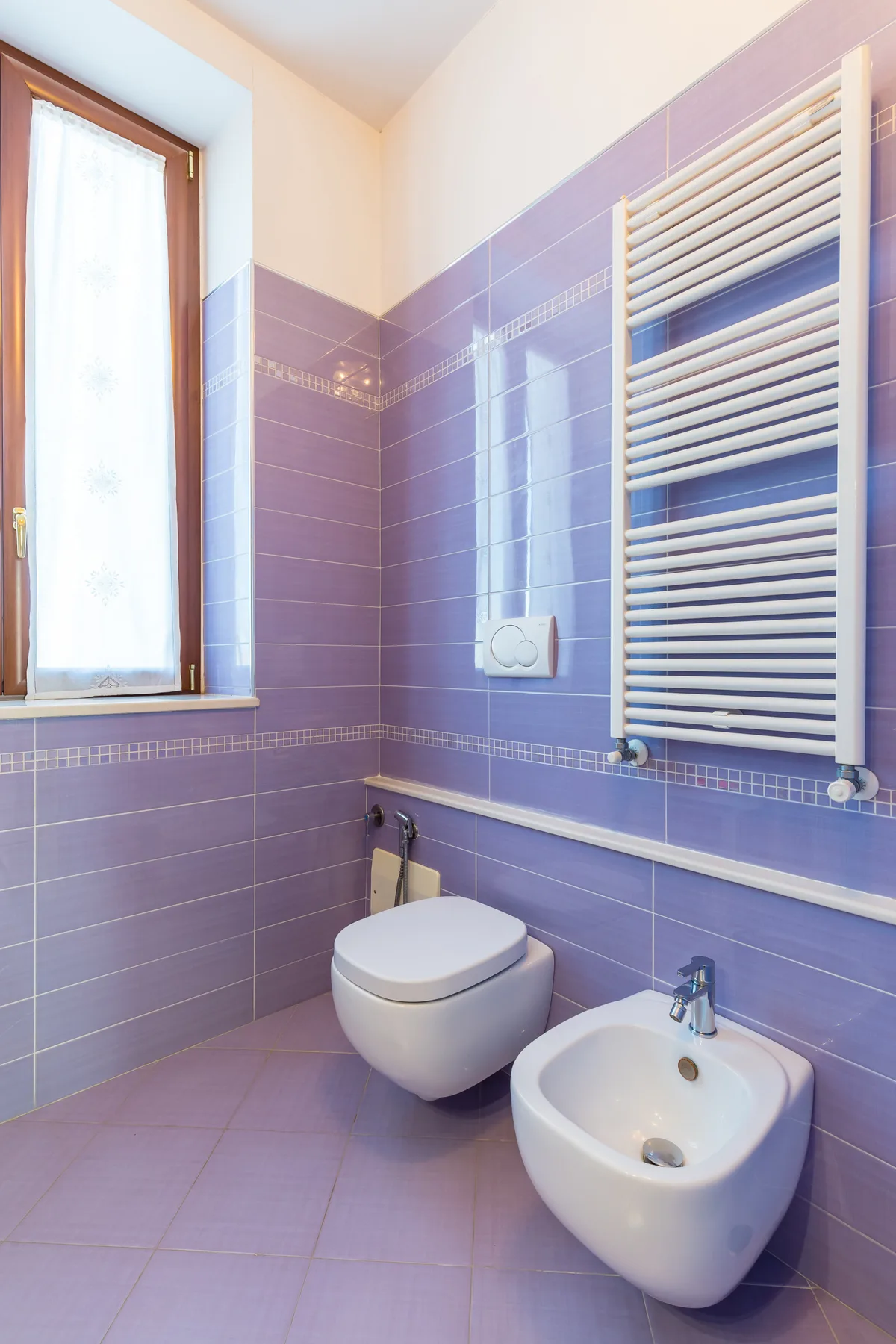 A purple-tiled bathroom with a toilet, bidet, and wall-mounted towel radiator.