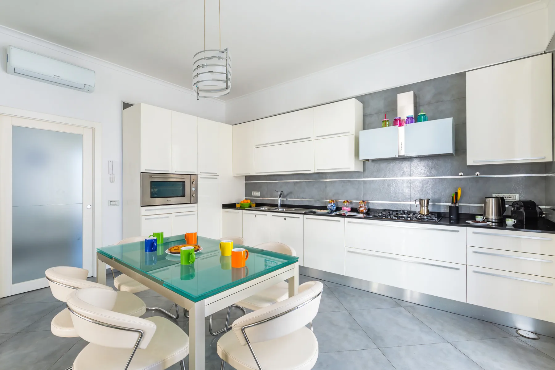 A modern kitchen with white cabinets and a glass dining table.