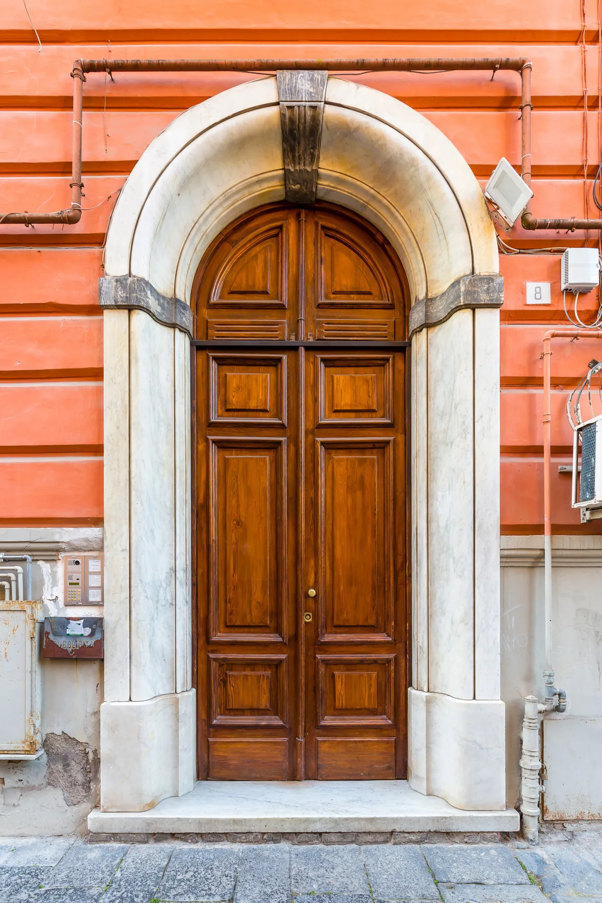 An ornate wooden double door set within a pale stone arch on a coral-colored facade.