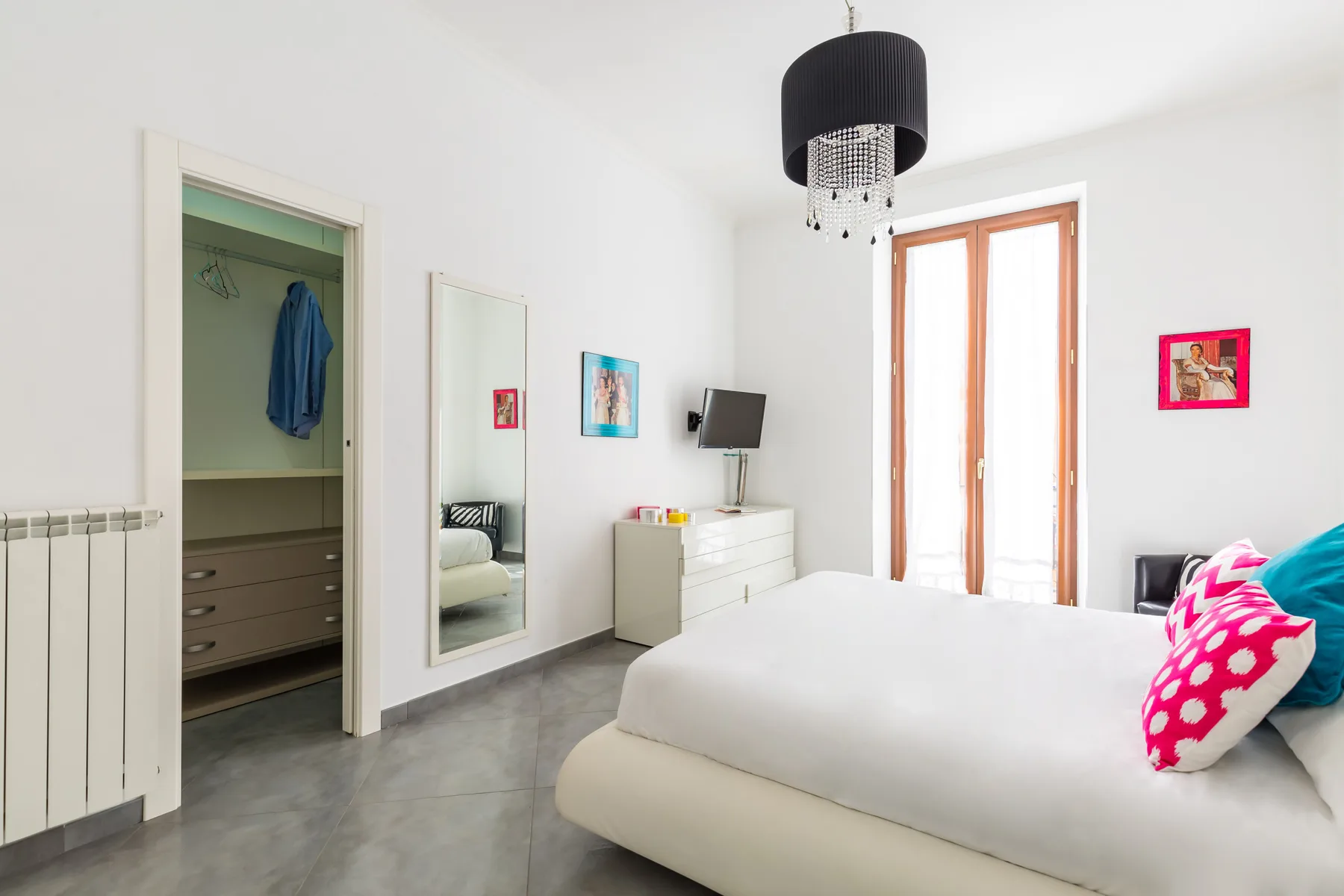 A bright bedroom with a large bed, dresser, and tall windows.