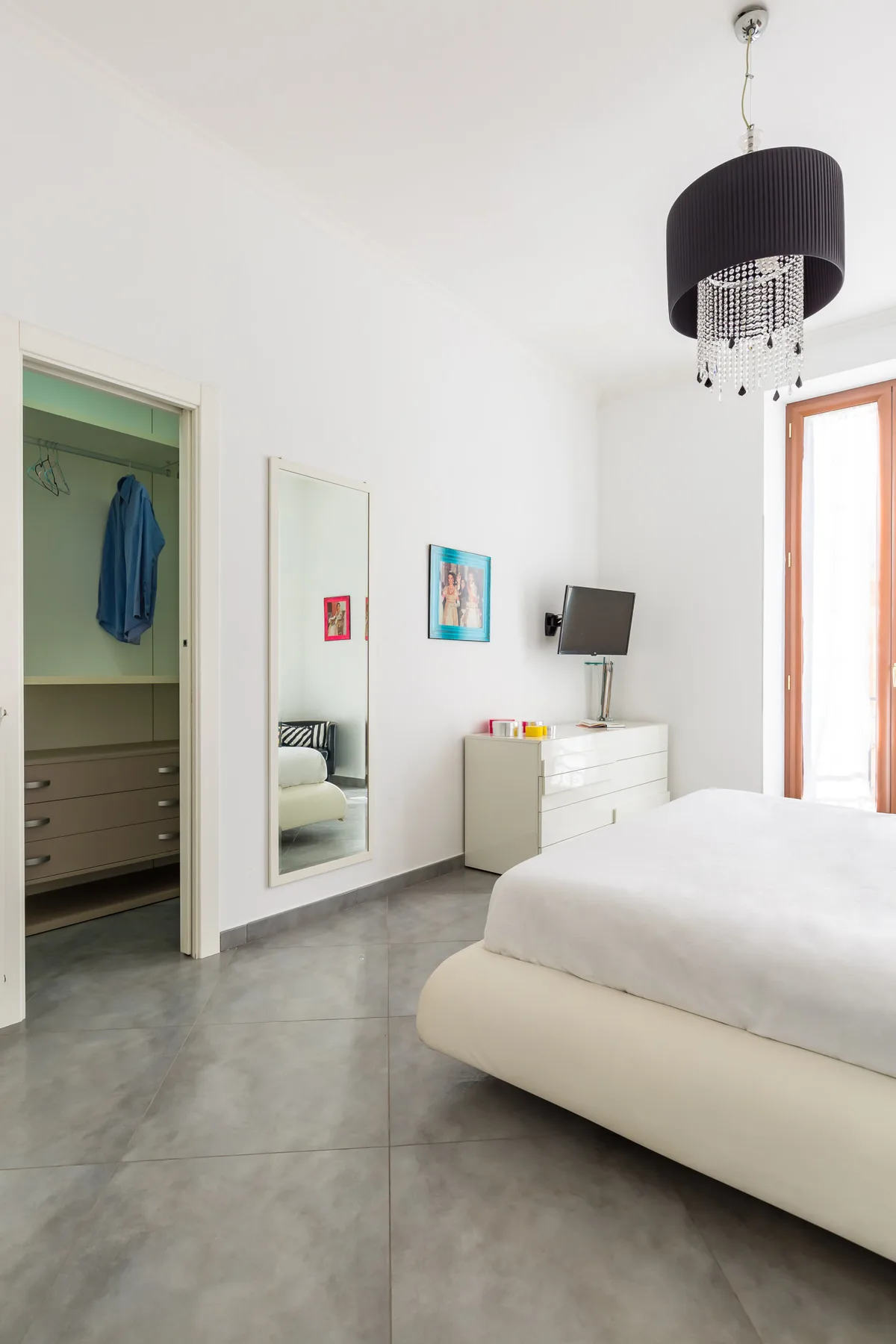 A bright bedroom with a large bed, dresser, and full-length mirror.