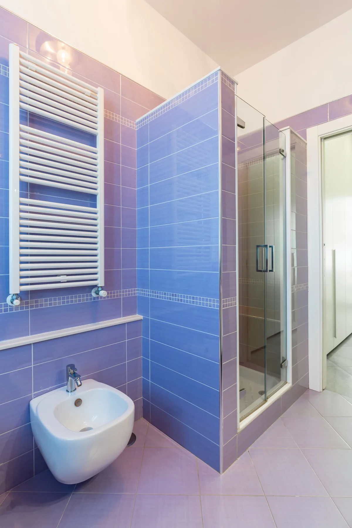 A tiled bathroom with a glass shower, wall-mounted radiator, and bidet.