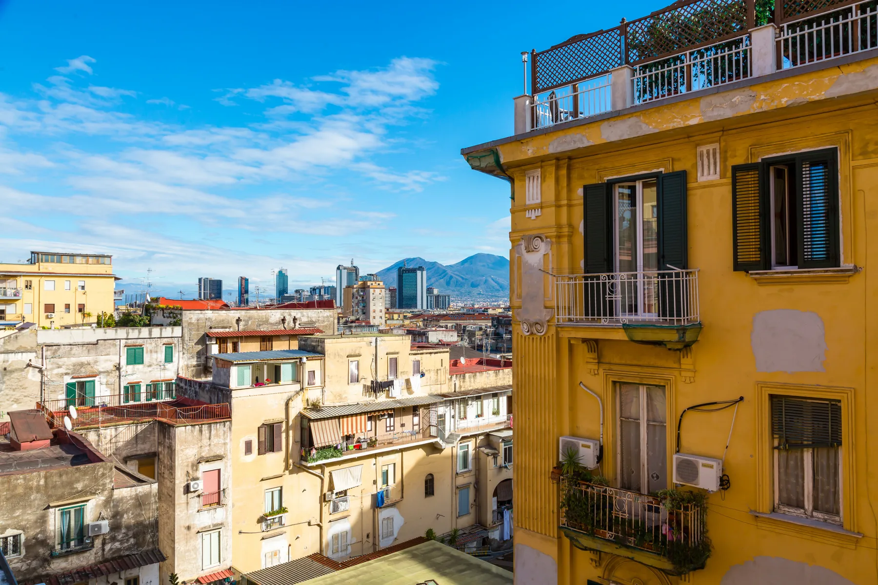 City buildings fill the view, with a yellow facade and distant mountains beneath a blue sky.