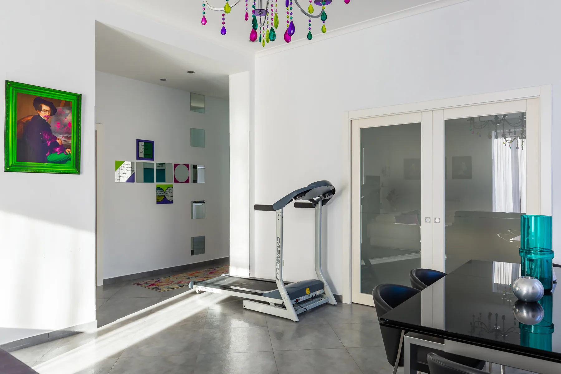 A bright interior room with a treadmill beside glass doors and a dining table.