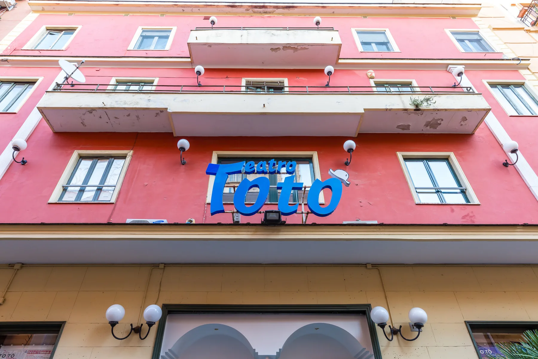 A pink building facade with balconies and a large blue sign above the entrance.