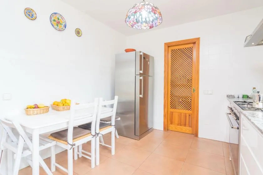 A bright kitchen with a dining table, refrigerator, and cabinets.