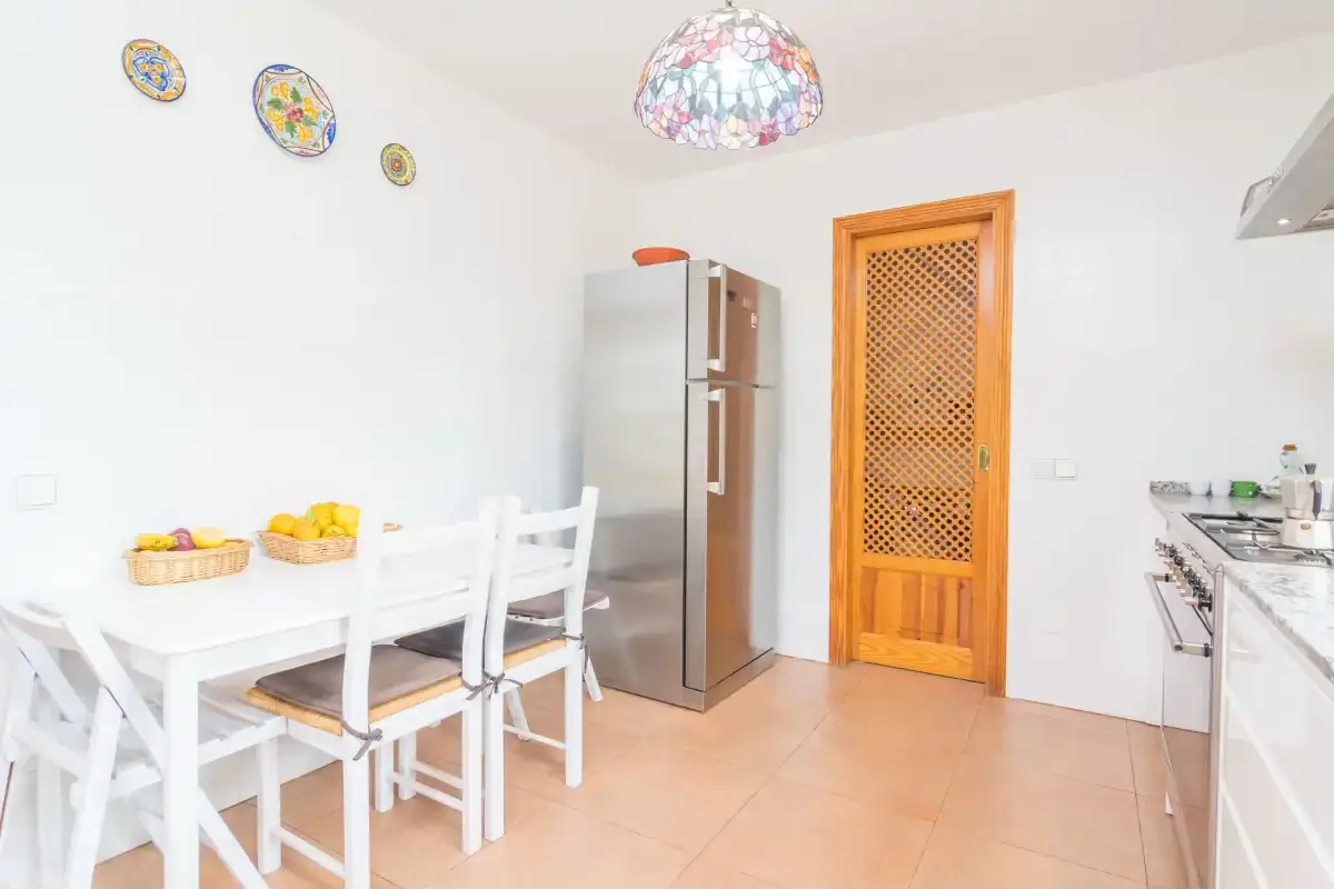 A bright kitchen and dining area with a white table beside the refrigerator.