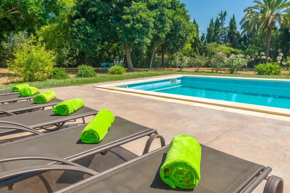 A swimming pool beside a paved patio with lounge chairs and green towels.