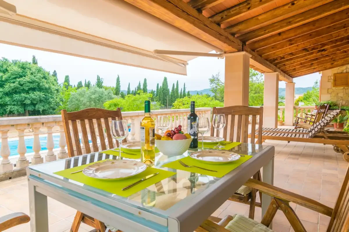 Covered outdoor dining area with a glass table set beside a balustrade.