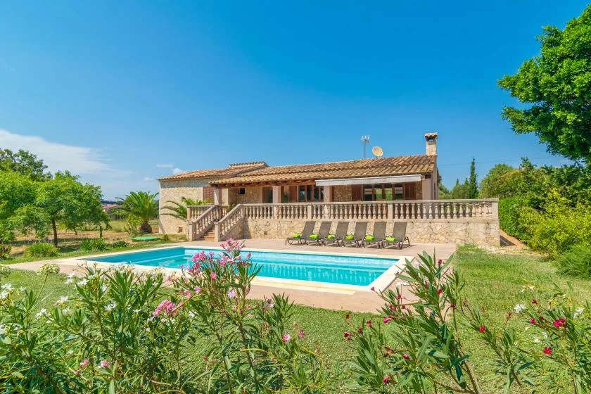 A swimming pool sits in front of a stone house surrounded by greenery.