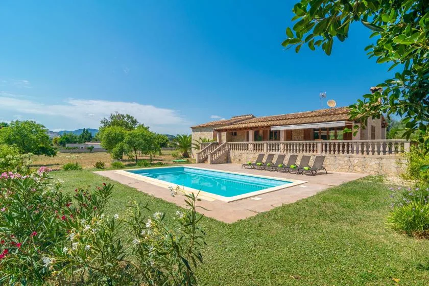 A swimming pool sits beside a tiled-roof house in a landscaped garden.