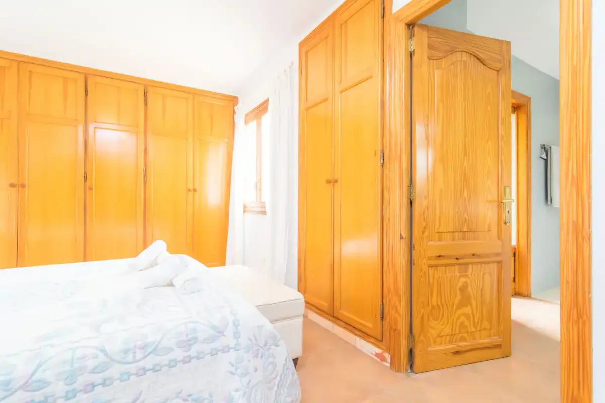 A bedroom with a bed, wooden wardrobes, and an open wooden door.