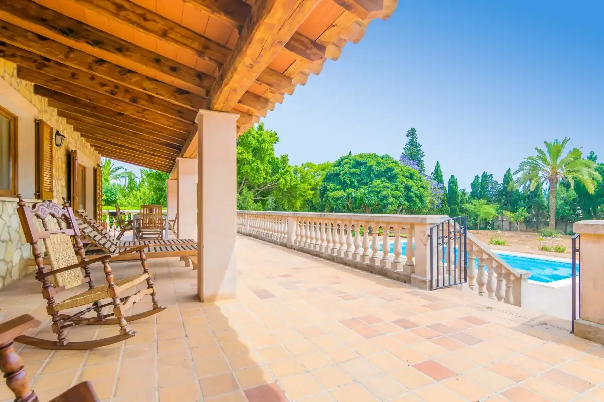 A covered terrace with seating overlooks a pool and leafy outdoor surroundings.